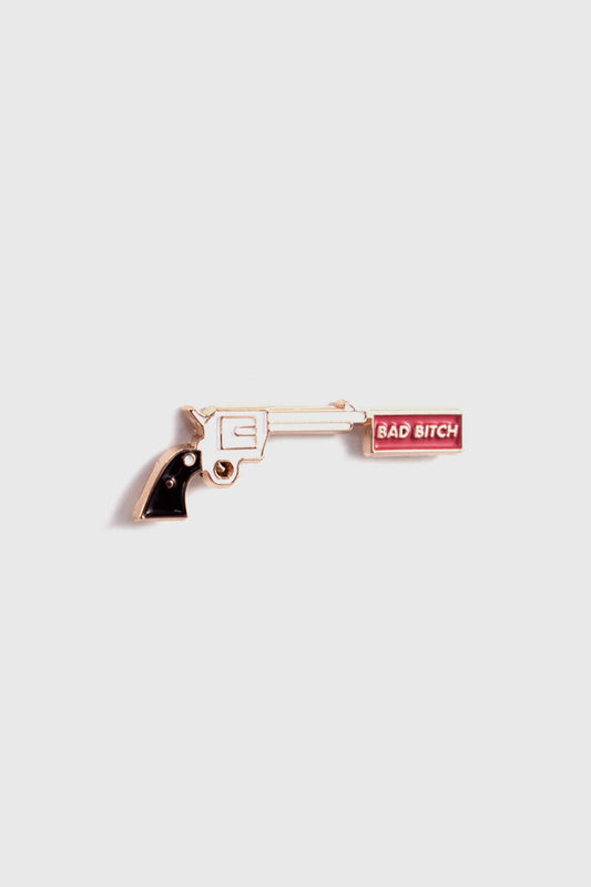 The Bad Bitch Pin by Badaboöm Studio, featuring a gold gun with a red banner that reads "Bad Bitch", is shown against a white background. 
