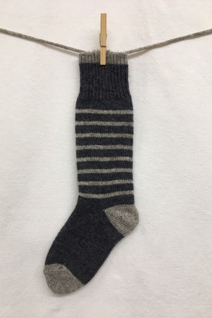 Knitted Socks by Charlevoix Pure Laine in Charcoal/Grey stripe are shown hanging on a clothesline against a white background