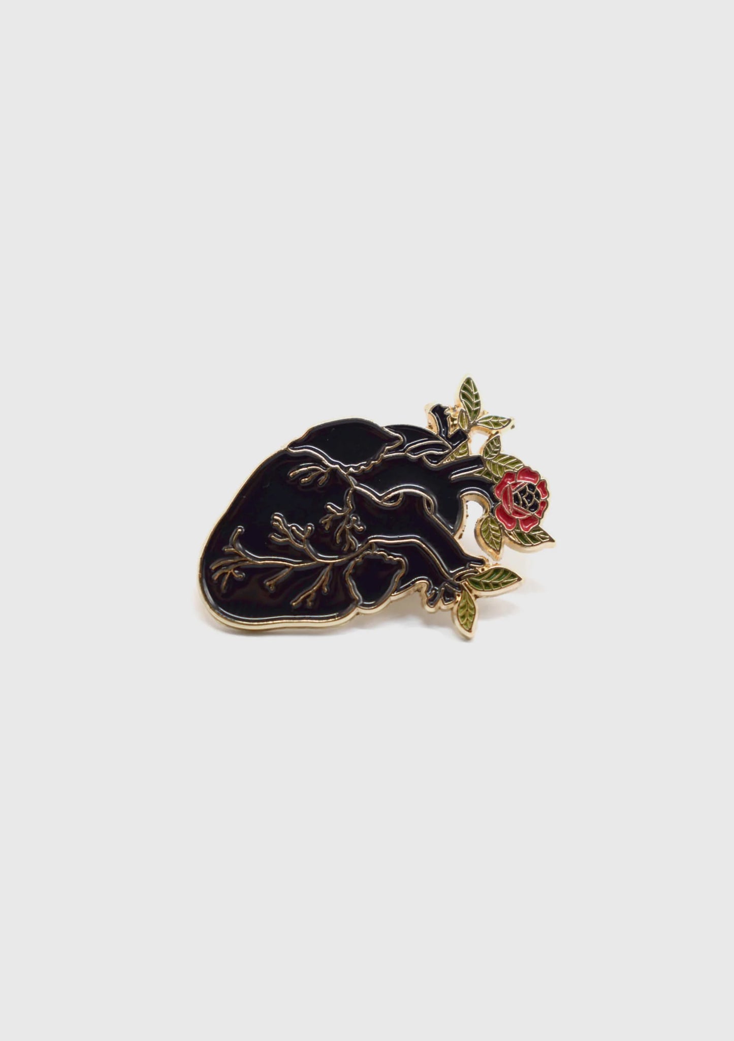 The Heart Flower Pin by Badaboöm Studio, featuring a black anatomically correct heart with flowers growing out of it, is shown against a white background. 