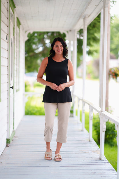A woman wearing the Vino 3/4 Pants from Rien ne se Perd in Natural, elastic waisted pants with large pockets, and slim 3/4 legs with side slits with coconut button details. She is wearing them with a black tank and standing on a porch. 