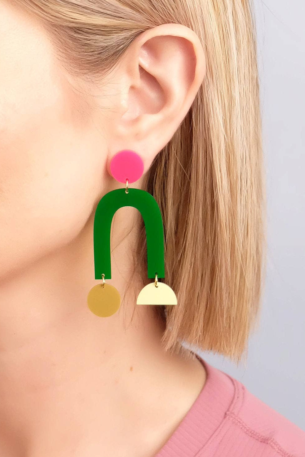 Earring with pink top, green middle, and gold bottom on a blurred background