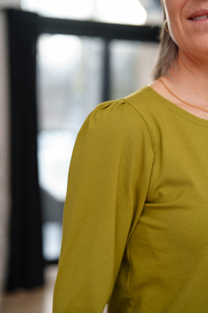 Close up of a woamn  wearing the Becancour Top by Rien ne se Perd in Pistachio, with a round neck and long slightly puffed sleeves with gathered cuffs.