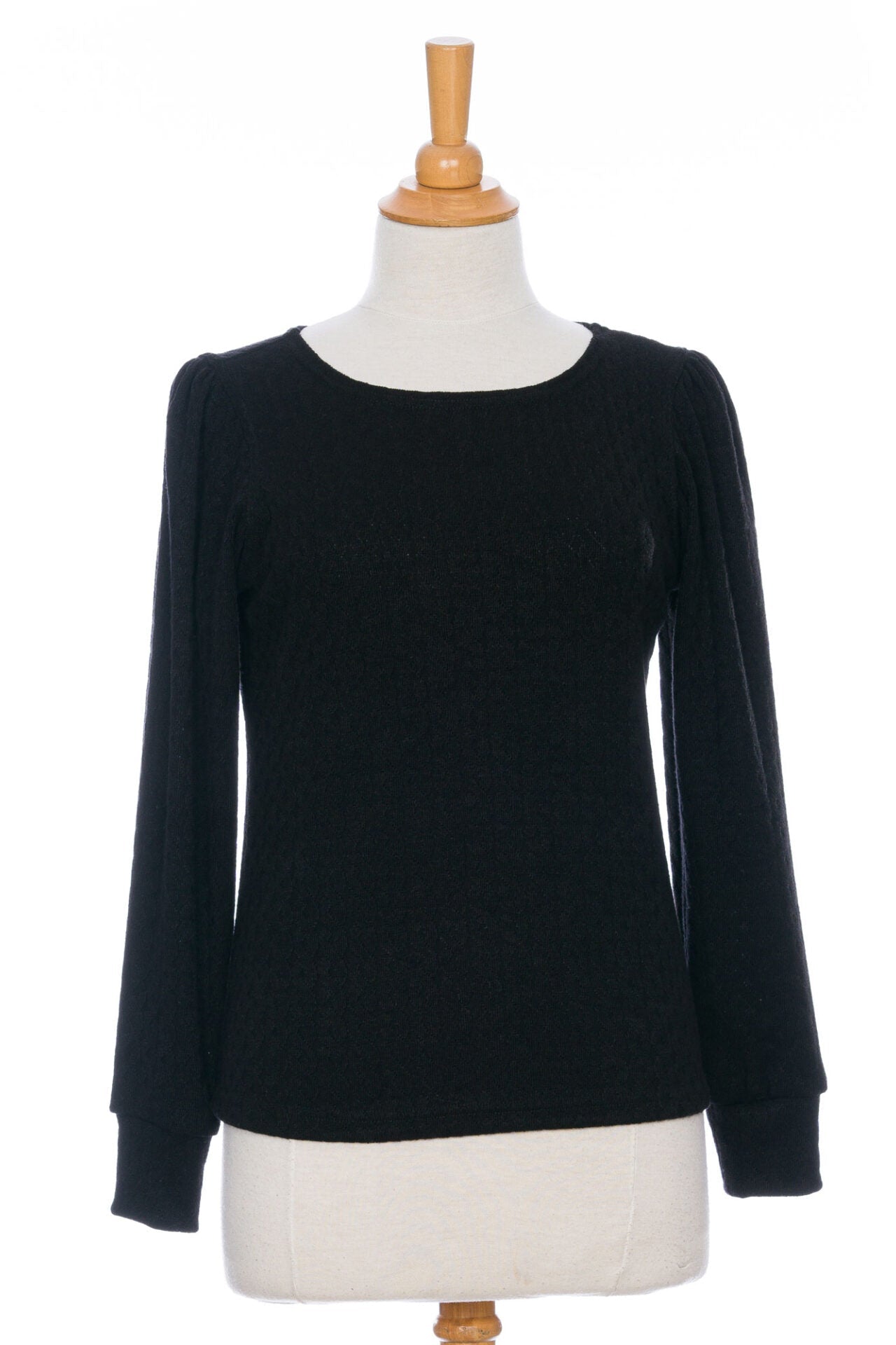 The Camarine Sweater by Rien ne se Perd in Black, a cable knit sweater with a scooped neck, puffed shoulders, and gathered cuffs, shown on a mannequin agains a white background. 