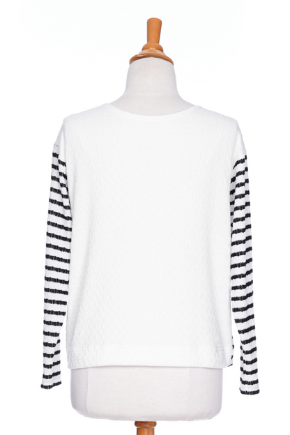 The Collins Reversible Sweater by Rien ne se Perd in Black/White is shown on a mannequin agains ta white background. t's reversible back to front with stripes on side and solid fabric on the other. It has long striped sleeves and a round neck. 