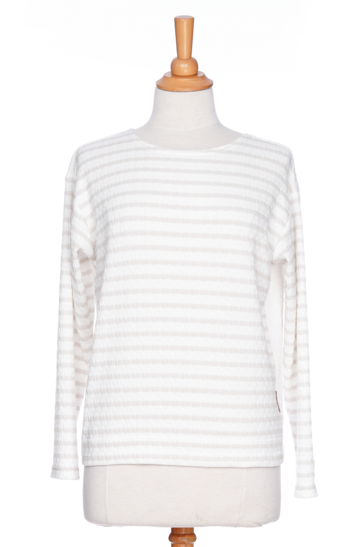The Collins Reversible Sweater by Rien ne se Perd in Sand/White is shown on a mannequin agains ta white background. t's reversible back to front with stripes on side and solid fabric on the other. It has long striped sleeves and a round neck. 