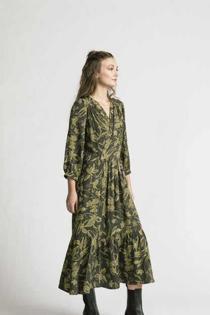 Side view of woman wearing the Chatterley Dress by Allison Wonderland in Green Floral, standing in front of a white background 