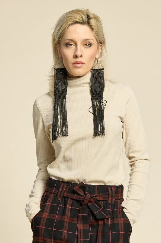 A woman wearing the Solo Top by Cokluch in Sand, a fitted turtleneck with a tone on tone striped, textured fabric and a twist detail at the neck. She is wearing it with the West Coast pants in Burgundy Plaid and standing in front of a beige background. 