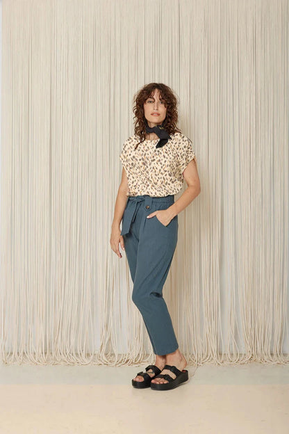 A woman wearing the Ombre Top by Cokluch in Watercolour print, featuring a round neck, short dropped sleeves, and a loose fit, with the teal pants, standing in front of a white background.