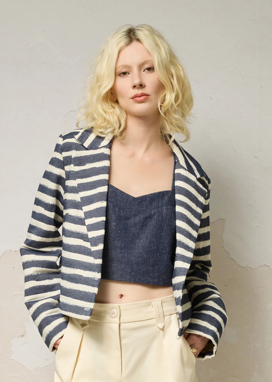 A woman wearing the Vesta Jacket by Cokluch in Denim Stripe over a denim top and beige pants against a plain background