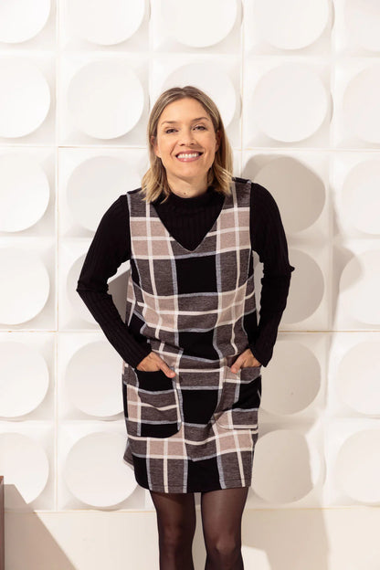 3/4 view of a woman wearing the Dolly Dress by Cherry Bobin in Checkered print, standing in front of a white wall 