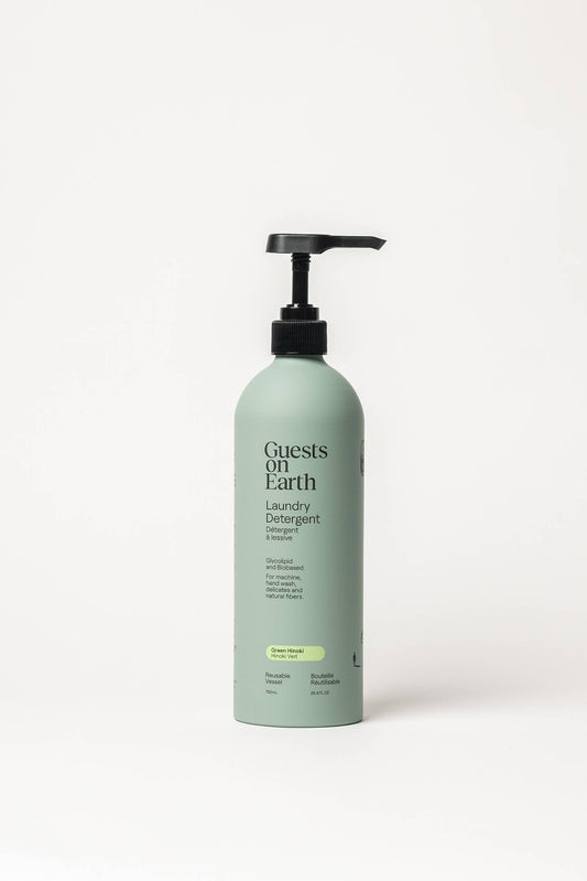 A bottle of Guests on Earth Laundry Detergent in a pale sage green color with a black pump dispenser, set against a plain white background.