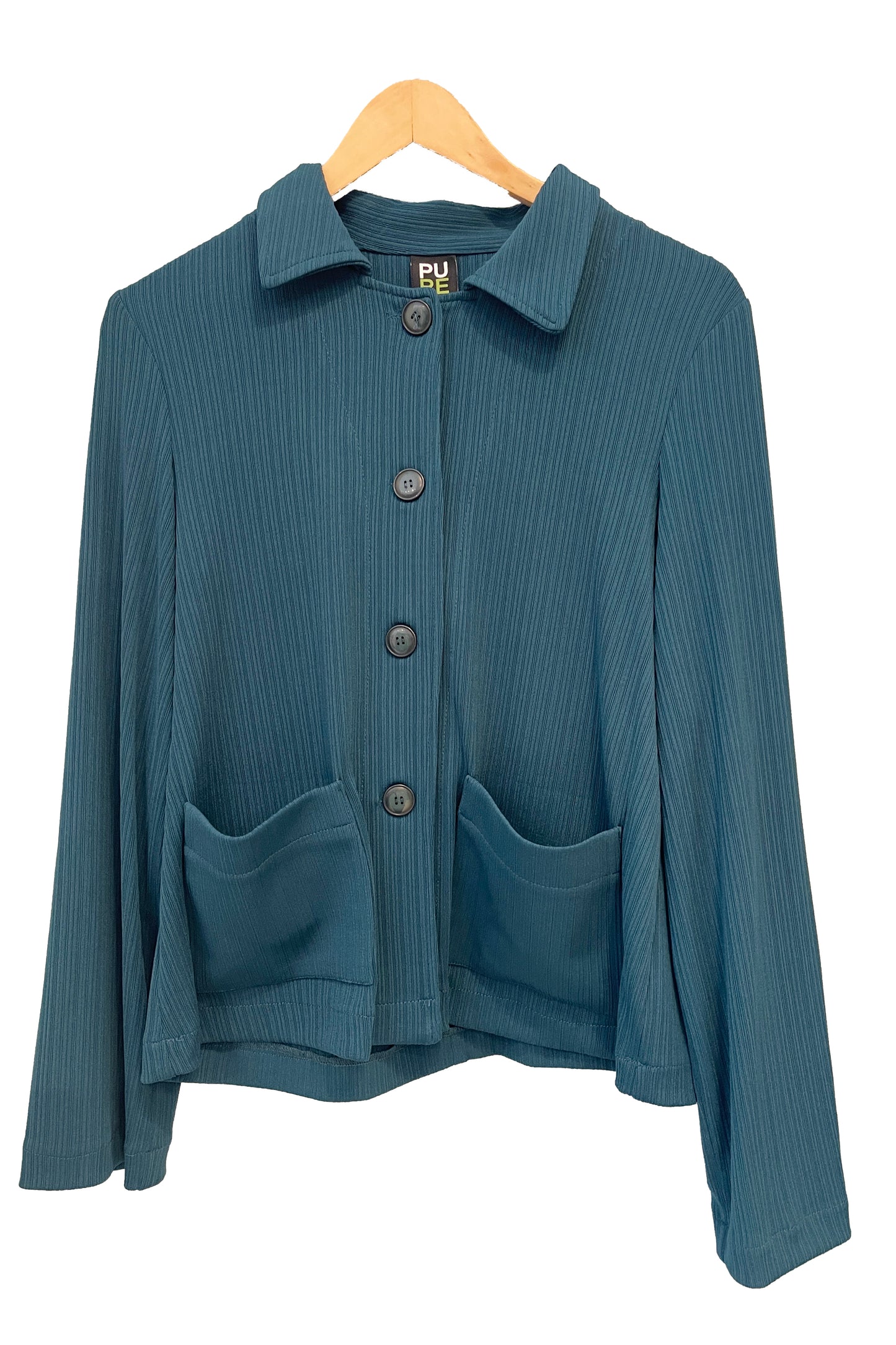 The Fern Jacket by Pure Essence in Spruce, a boxy jacket with a lapel collar, button front and patch pockets in a ribbed fabric, is shown hanging in front of a white background. 