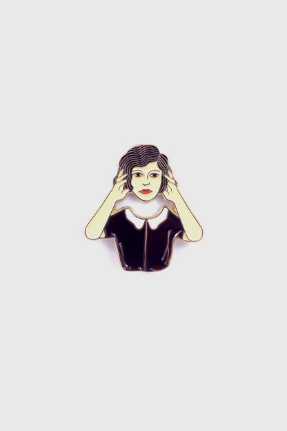 The Floating Head Pin by Badaboöm Studio, an enamel pin showing a woman lifting her head over her shoulders, is shown against a white background. 