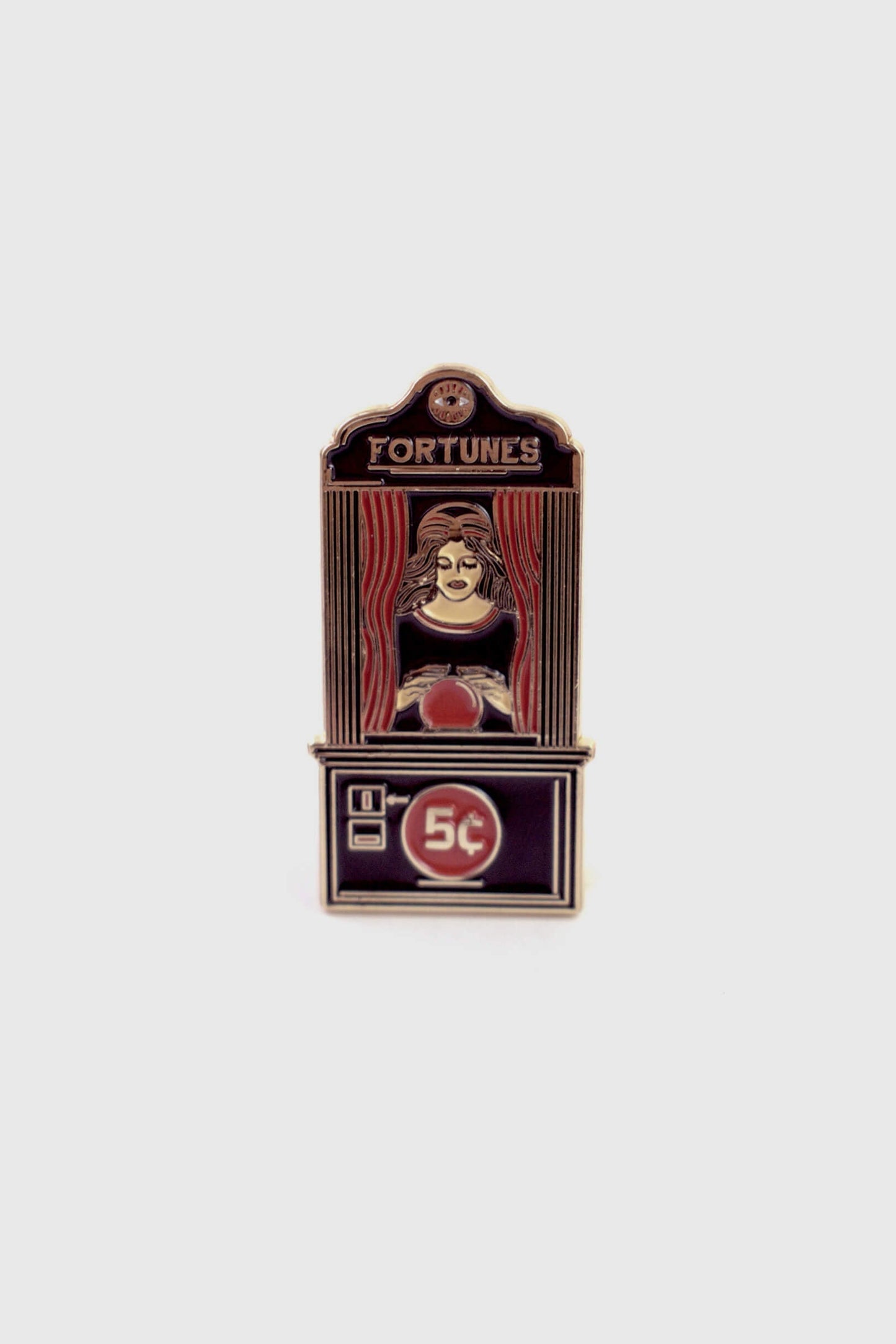 The Fortune Teller Pin from Badaboöm Studio is an enamel pin shaped like a vintage fortune telling booth with the word 'FORTUNES' at the top and '5c' on the lower panel. It's shown against a white background. 