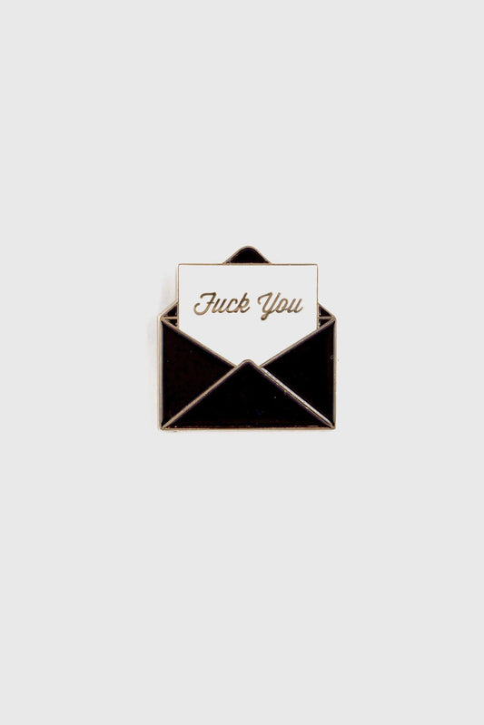 The Fuck You Pin by Badaboöm Studio, featuring a black envelope and white piece of paper that reads "fuck you" in gold lettering, is shown against a white background. 