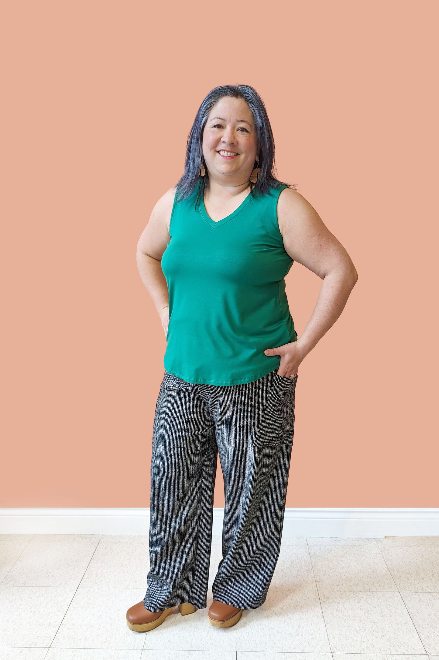 Christina wearing the Charlotte Camisole  by Pure Essence in Emerald with the Bakairi Pants by Kollontai, standing in front of a coral wall