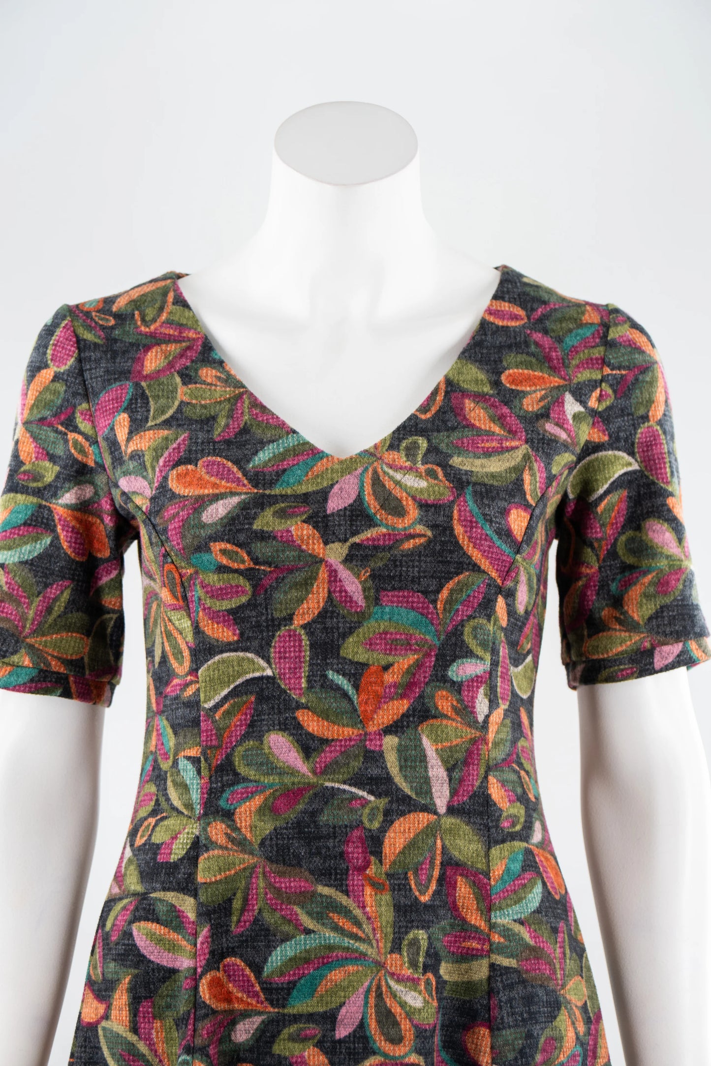The Botanical Dress by Karkass in Floral, a knit dress with a V-neck, elbow length sleeves, fit and flare shape, and above the knee hem, is shown on a mannequin in front of a white background. 