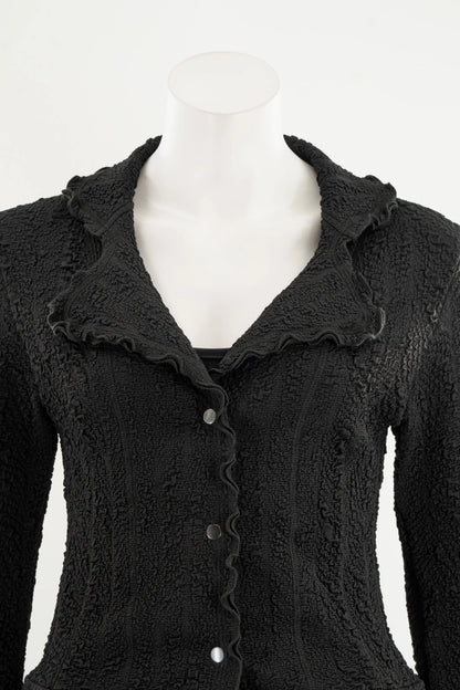 The Essential Jacket - Jasper by Karkass is shown on a mannequin in front of a white background. It's a black textured jacket with a ruffled collar, button closure, and frill details at the cuffs and hem. 