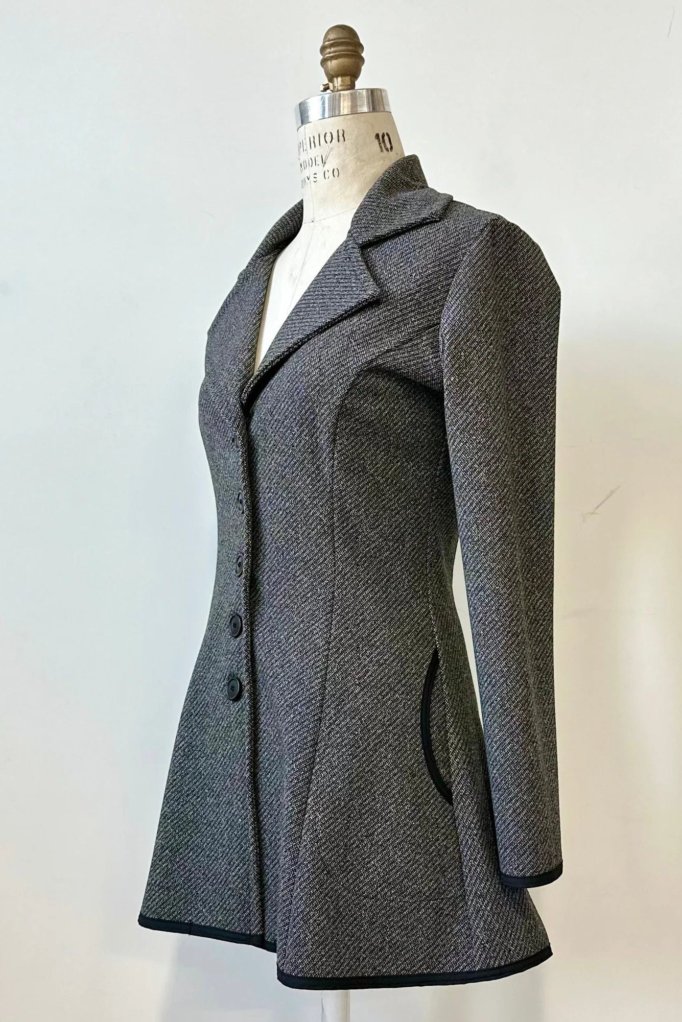 Side view of the Henderson Jacket by Kollontai in Charcoal tweed, with a fitted A-line shape that flares from the waist, a classic collar, and buttons down the front, shown on a mannequin in front of a white background. 