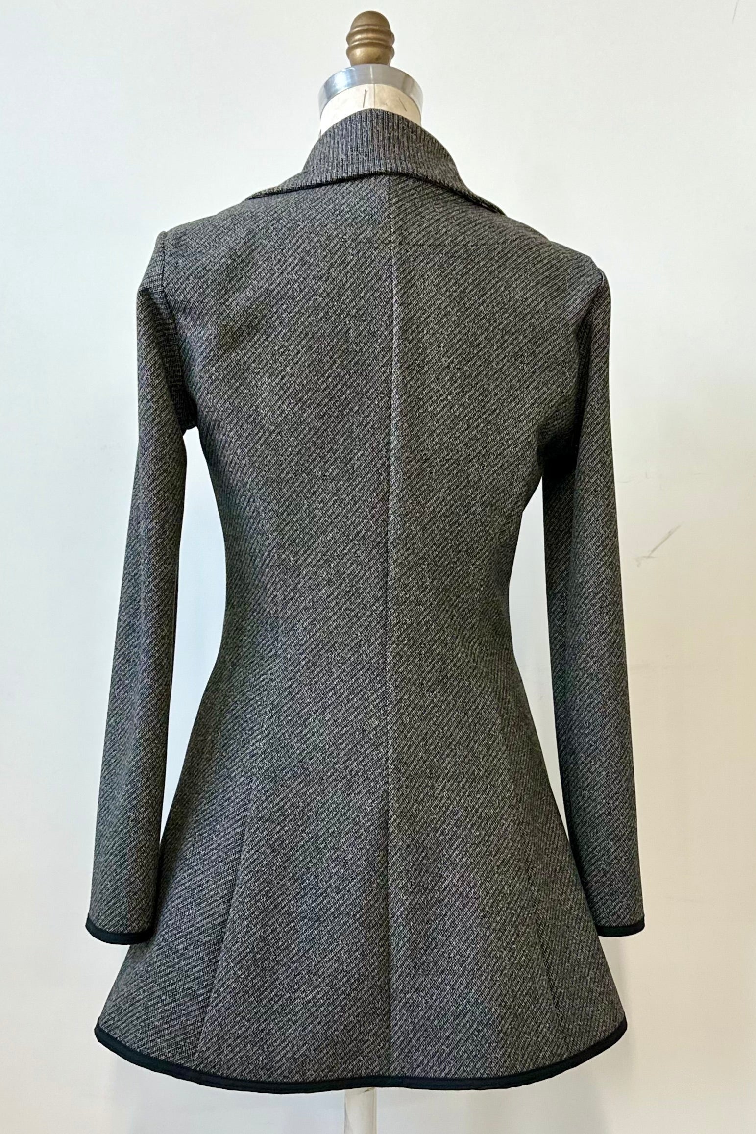 Back view of the Henderson Jacket by Kollontai in Charcoal tweed, with a fitted A-line shape that flares from the waist, a classic collar, and buttons down the front, shown on a mannequin in front of a white background. 