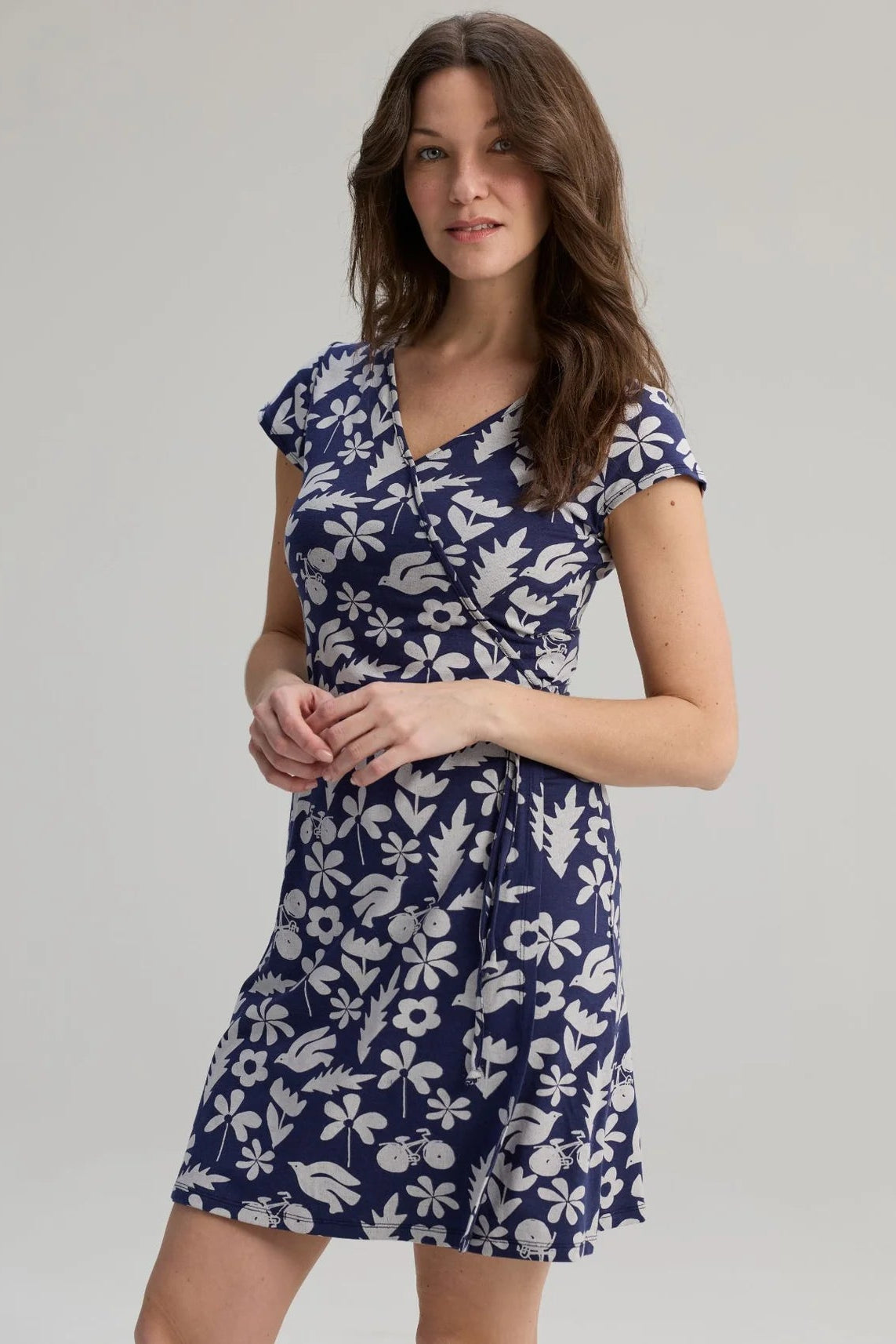 A woman wearing the Libellule Dress by Message Factory in Blue Print, a short sleeved wrap dress that falls to the knee. She is standing against a plain background. 