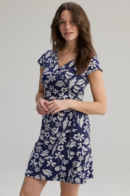 A woman wearing the Libellule Dress by Message Factory in Blue Print, a short sleeved wrap dress that falls to the knee. She is standing against a plain background. 