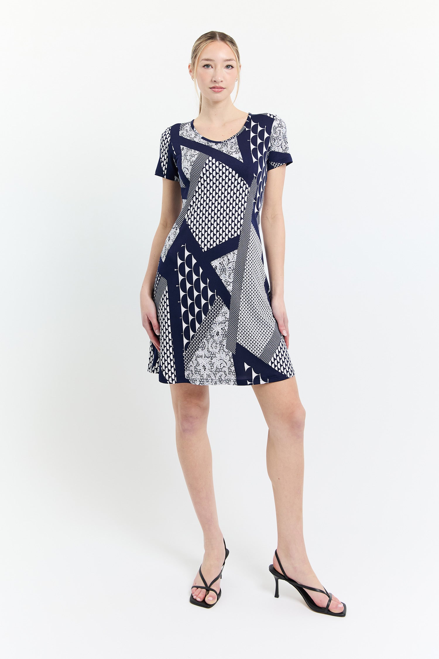 A woman wearing the Work Dress by Dinh Ba in Blue and White Graphic print, with a round neck, short sleeves, and A-line shape that hits above the knee. She is standing in front of a white background. 