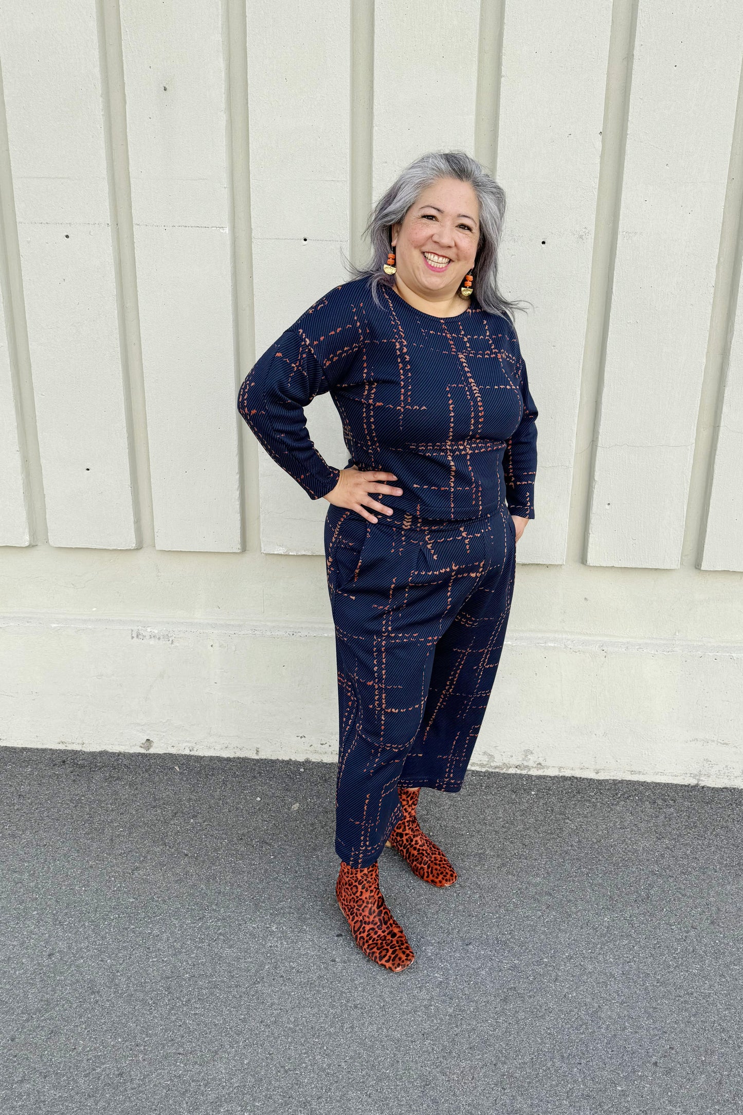 A woman wearing the Jackson Top and Julian Pants by Melow in Indigo, standing outside in front of a white wall