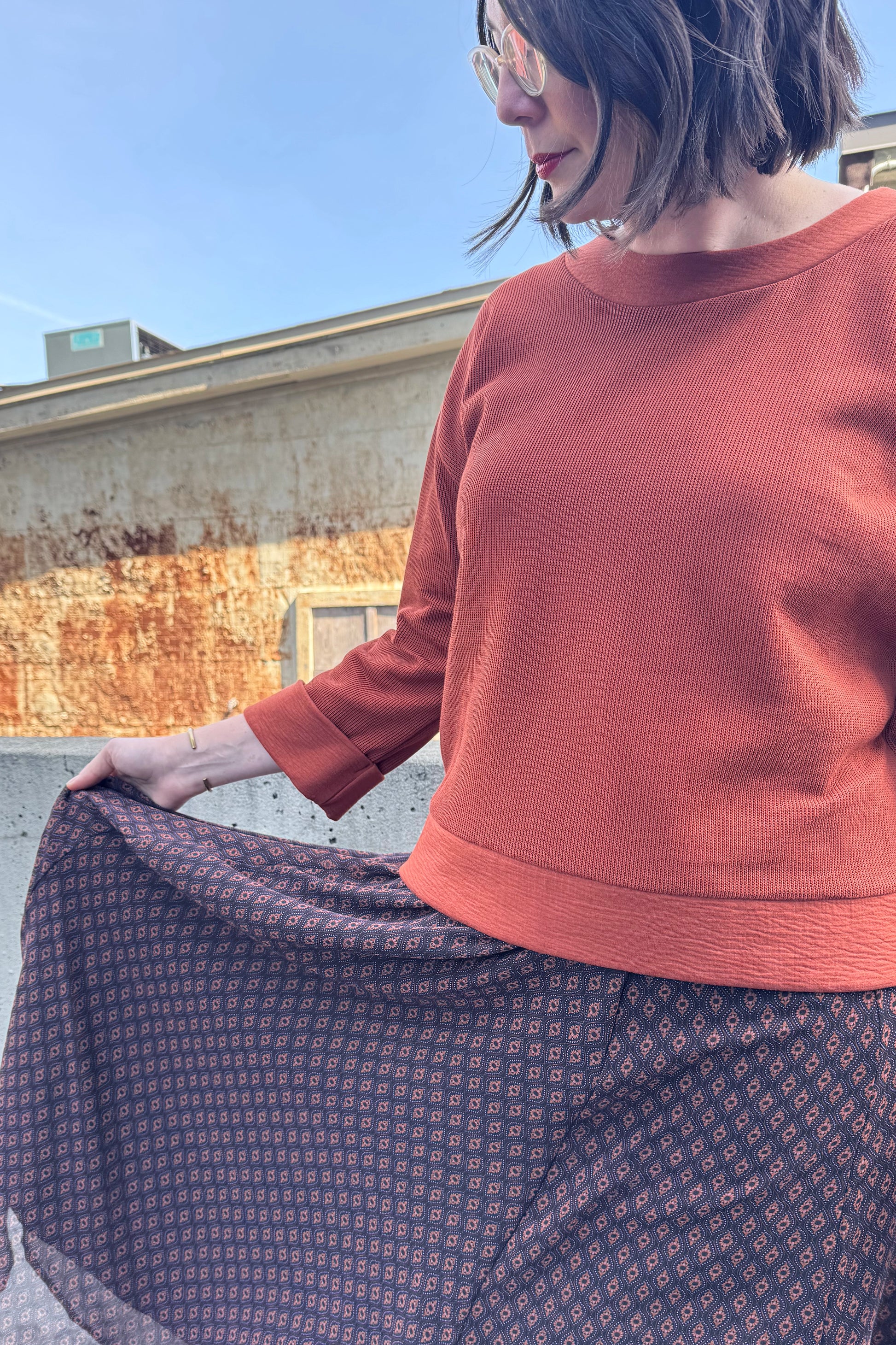 Close up detail of a woman wearing the Espresso Skirt by Cherry Bobin in Black and Brown print, a long and flowing chiffon skirt that's fully lined. She's wearing it with the Mocha Sweater in Bronze and standing outside in front of a brick building.
