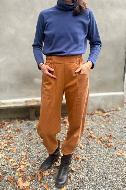 A woman wearing the Oris Raglan Turtleneck by Kazak in Indigo waffle. She is wearing it with yellow pants and standing outside. 