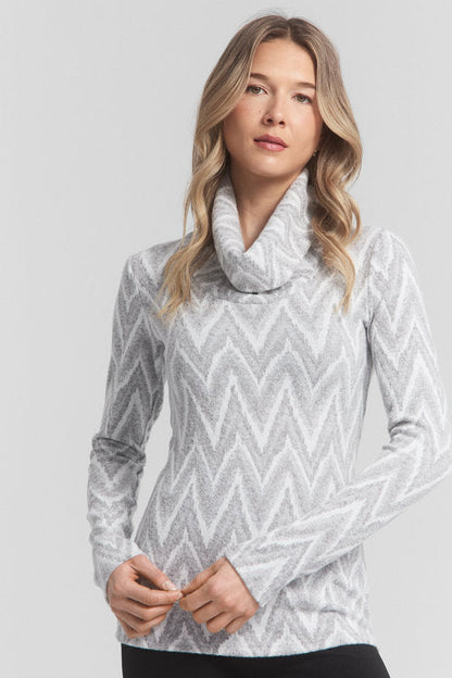 Waist up view of a woman wearing the Anne Top by Dinh Ba in White, a slim fitting top with a large turtleneck and a zigzag pattern. She is wearing it with black pant and standing in front of a white background. 