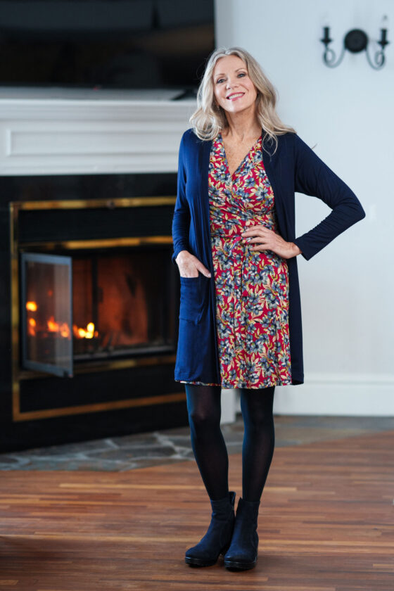 A woman wearing the Renoir Dress by Rien ne se Perd in Red Floral, standing in front of a fireplace