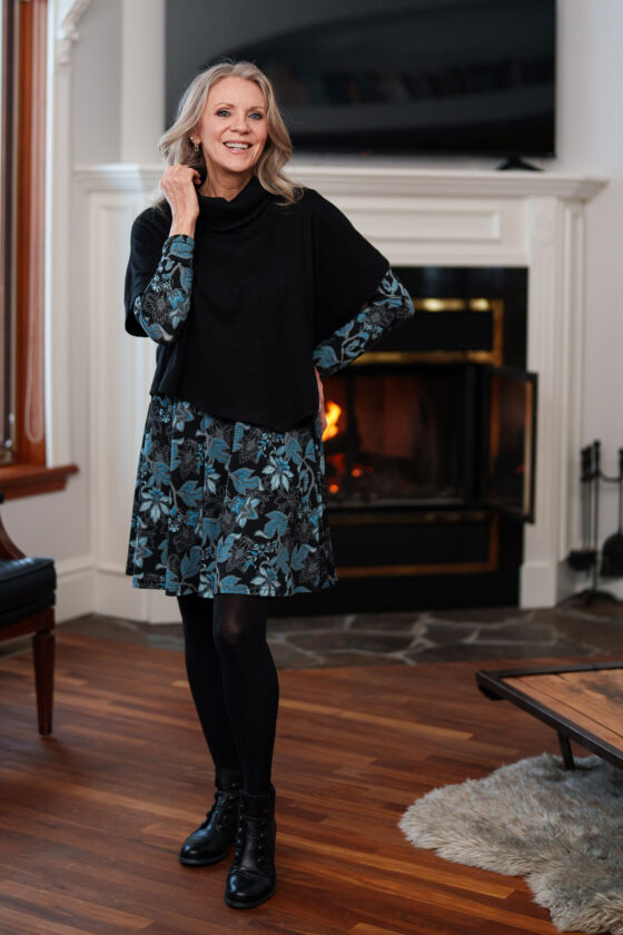 A woman wearing the Delacroix Bolero-Poncho by Rien ne se Perd in Black standing in front of fireplace