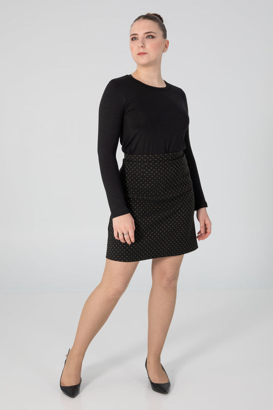A woman wearing the Eve Skirt by Slak in Golden X print on Black, an above the knee-length pull-on skirt with a slight A-line shape. She is wearing it with the A-25 sweater in Black and standing in front of a white background. 