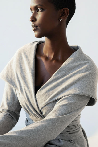 A woman wearing the Signature Cotton Hooded Wrap by Stacey Martin in Stone a hooded, corset waist sweatshirt with a tie belt,  against a white background. 
