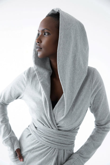 A woman wearing the Signature Cotton Hooded Wrap by Stacey Martin in Stone a hooded, corset waist sweatshirt with a tie belt. She is standing against a white background. 