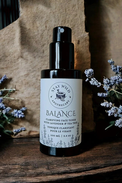 Bottle of 'Balance' face mist by Stay Wild Apothecary shown with lavender flowers on a wooden surface