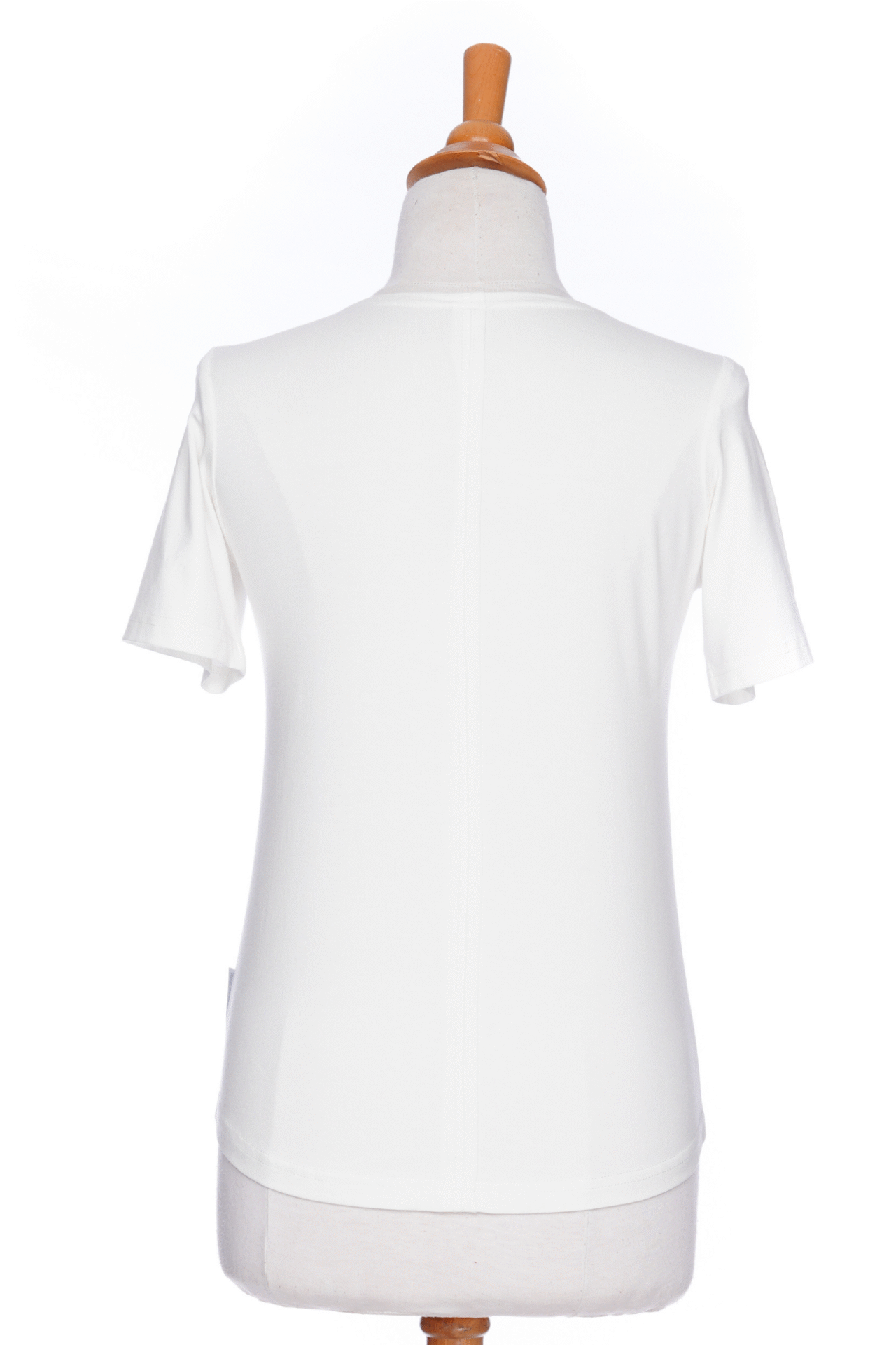 A back view of the Mai Tai T-shirt from Rien ne se Perd in Ivory, with coconut buttons at the shoulder, seam accents front and back, and a rounded hi-low hemline, is shown on a mannequin against a white background. 