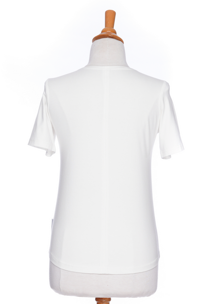 A back view of the Mai Tai T-shirt from Rien ne se Perd in Ivory, with coconut buttons at the shoulder, seam accents front and back, and a rounded hi-low hemline, is shown on a mannequin against a white background. 