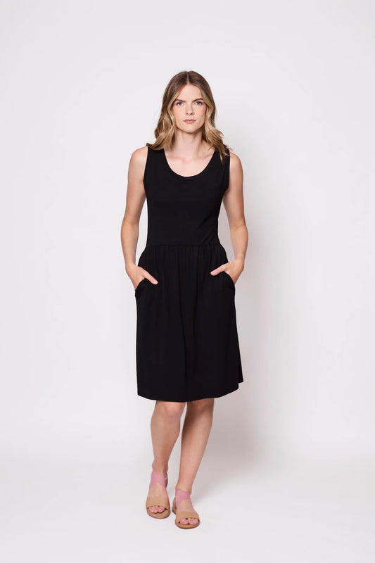 A woman wearing the Mai Dress by Tangente in Black,a  sleeveless dress with a scooped neck and gathered knee-length skirt. She is standing against a white background