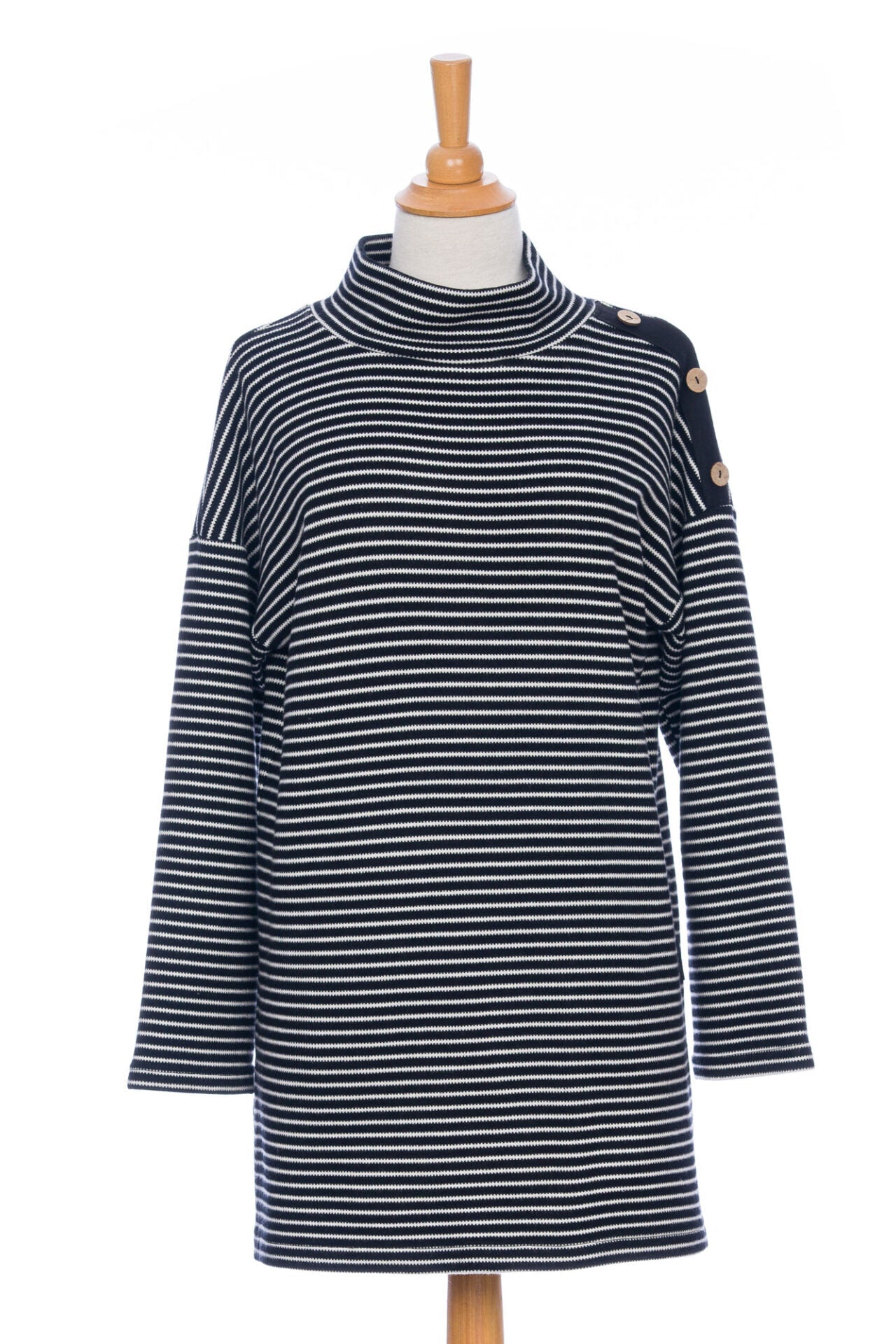 The Aralie Tunic by Rien ne se Perd in Black and White Stripe, with a high neckline, long sleeves, side slits for ease, drop sleeves and a coconut button placket on the left shoulder, is shown on a mannequin against a white background. 