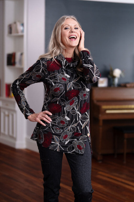 A woman wearing the Corno Tunic by Rien ne se Perd in Black and Red stands in front of a piano. 