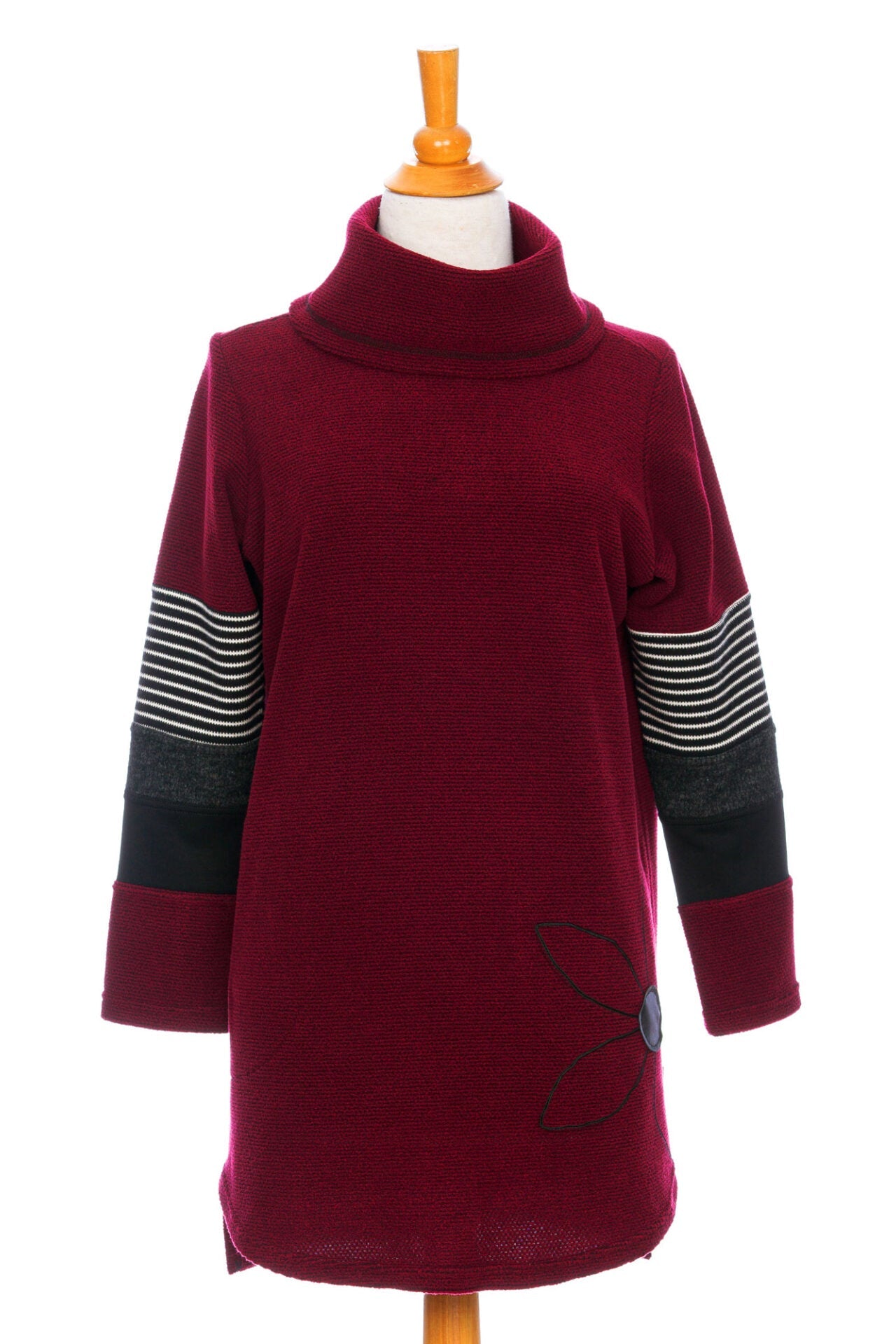 The Églantier Tunic by Rien ne se Perd in textured Bordeaux fabric with striped and black colour-blocking on the long sleeves is shown on a mannequin against a white background. It has a large turtleneck, a faux leather floral decal, and a side pocket. 