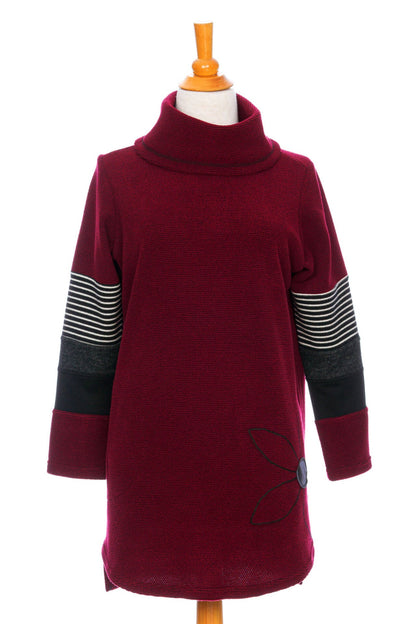The Églantier Tunic by Rien ne se Perd in textured Bordeaux fabric with striped and black colour-blocking on the long sleeves is shown on a mannequin against a white background. It has a large turtleneck, a faux leather floral decal, and a side pocket. 