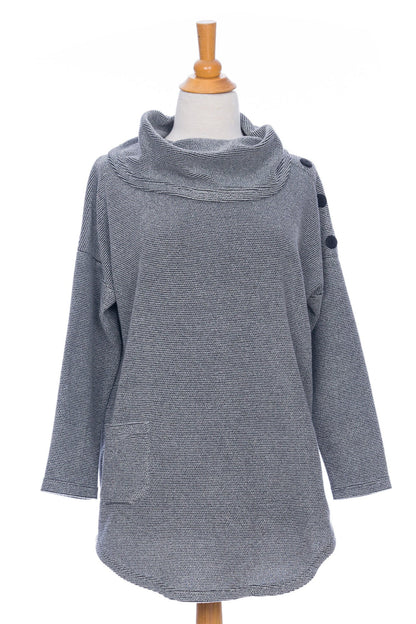 The Myrique Tunic by Rien ne se Perd in Grey, an oversized chenille tunic with a large cowl neck, rounded hem, faux leather elbow patches, button placket at the left shoulder, and patch pocket on the front, is shown on a mannequin in front of a white background. 
