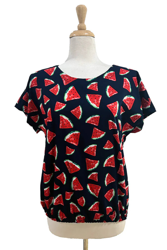 The Macaron Top by Desserts and Skirts in Watermelon, with a round neck, short sleeves, and a loose fit, is shown on a mannequin against a white background. 