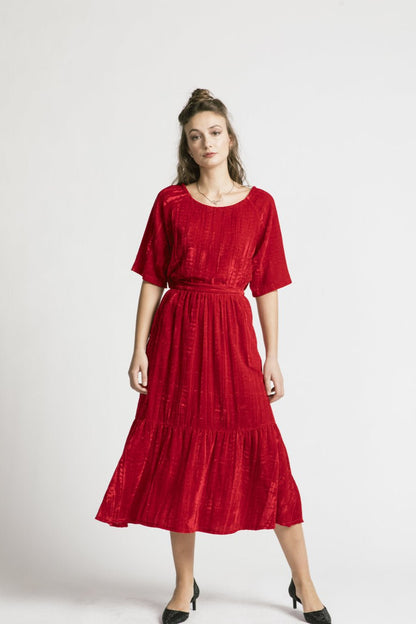 A woman wearing the Wuthering Top by Allison Wonderland in red crushed velvet, with a dark skirt, standing in front of a white background 