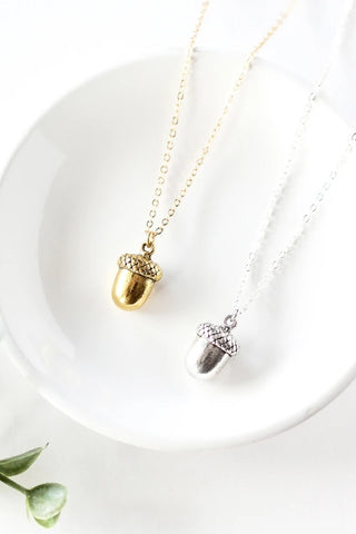 Tiny acorn necklace by Birch Jewellery, in silver and gold, styled on a white ceramic dish