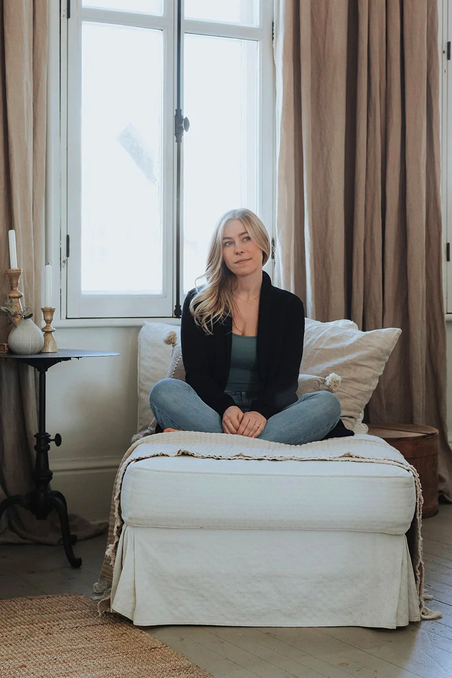 A woman wearing the Classic Briton Cardigan by Blondie Apparel in Black with jeans, sitting on a chaise lounge