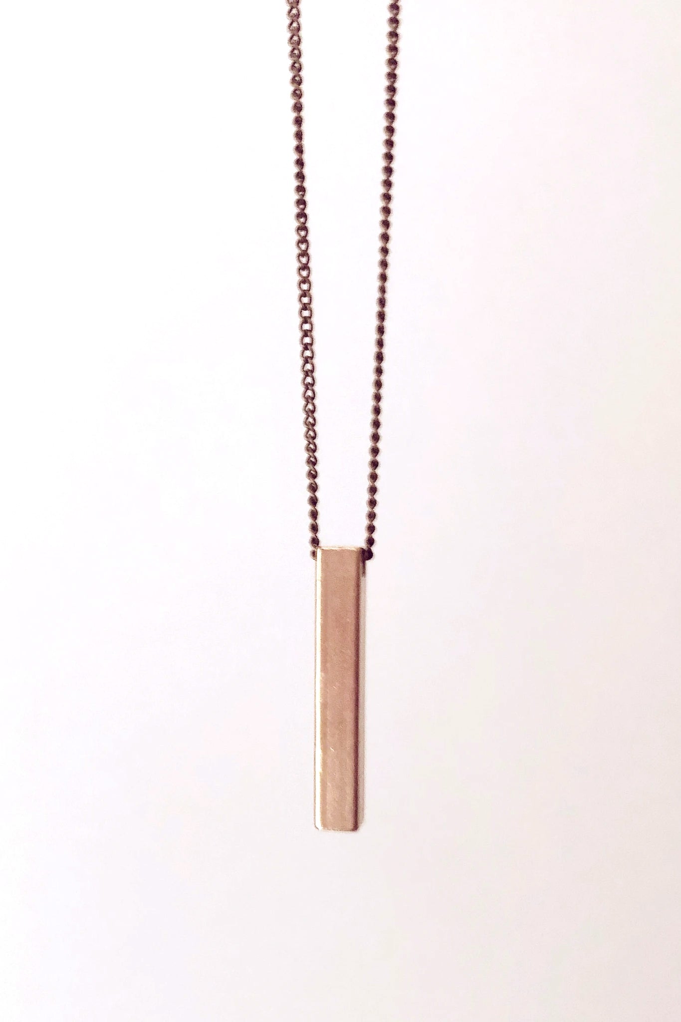 Gigi necklace by Darlings of Denmark; vertical solid bar detail; mid-length chain; close-up; raw brass; flat lay